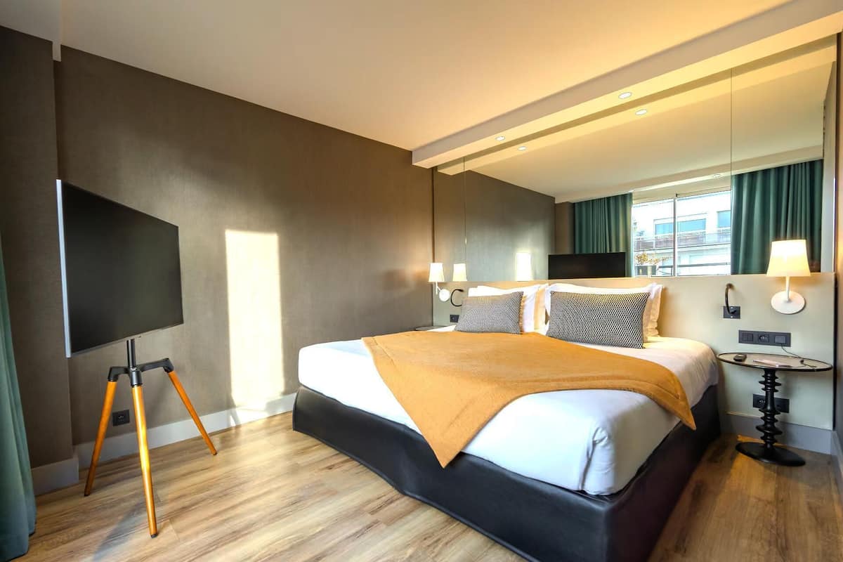 A modern hotel room with a large bed, a flat-screen TV, and a desk lamp.
