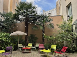 Une cour avec des sièges en plein air, un palmier et un bâtiment en arrière-plan.