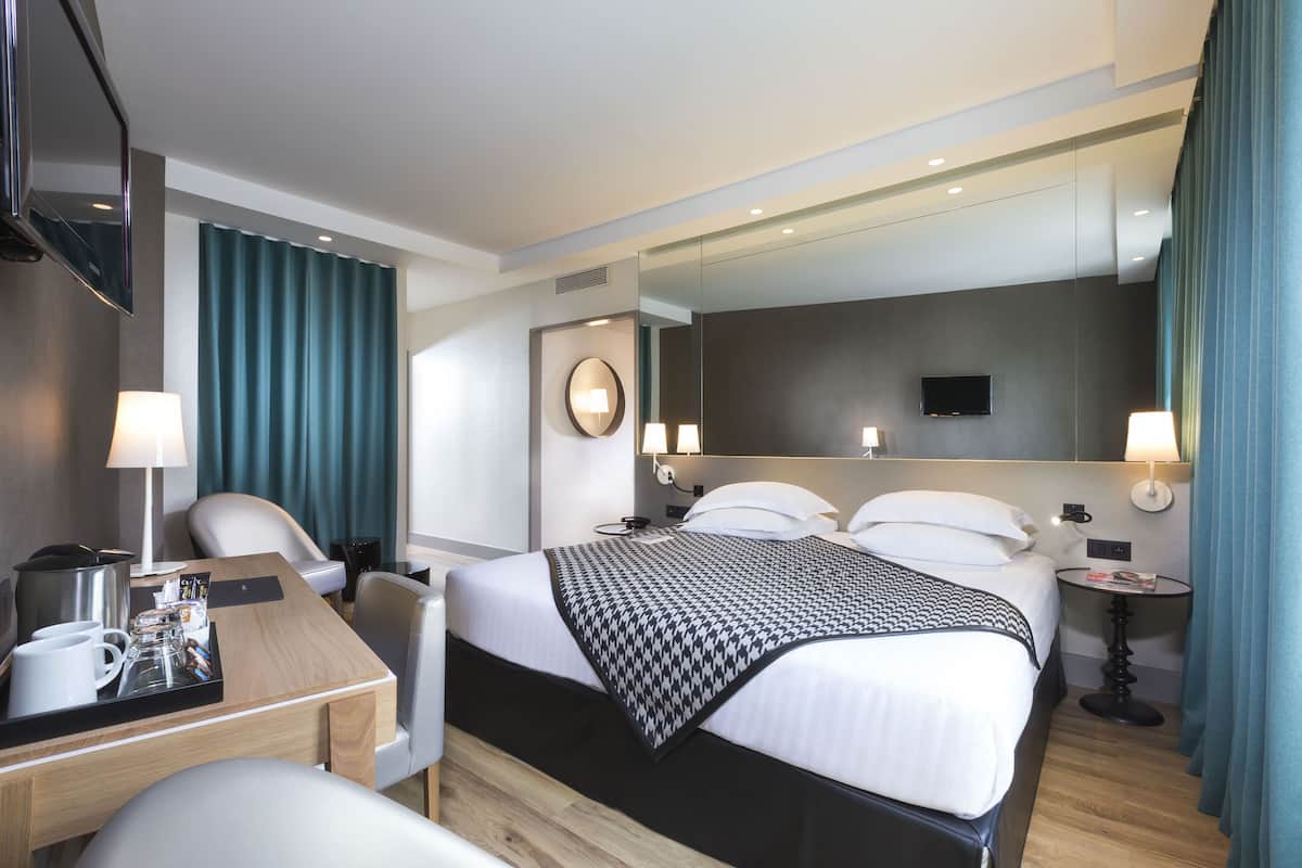 A modern hotel room with a neatly made bed, a desk with a coffee maker, and a television mounted on the wall.