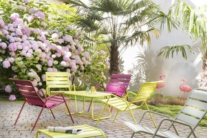 Un patio con mobiliario exterior, una palmera y una pared con arbustos de hortensia.