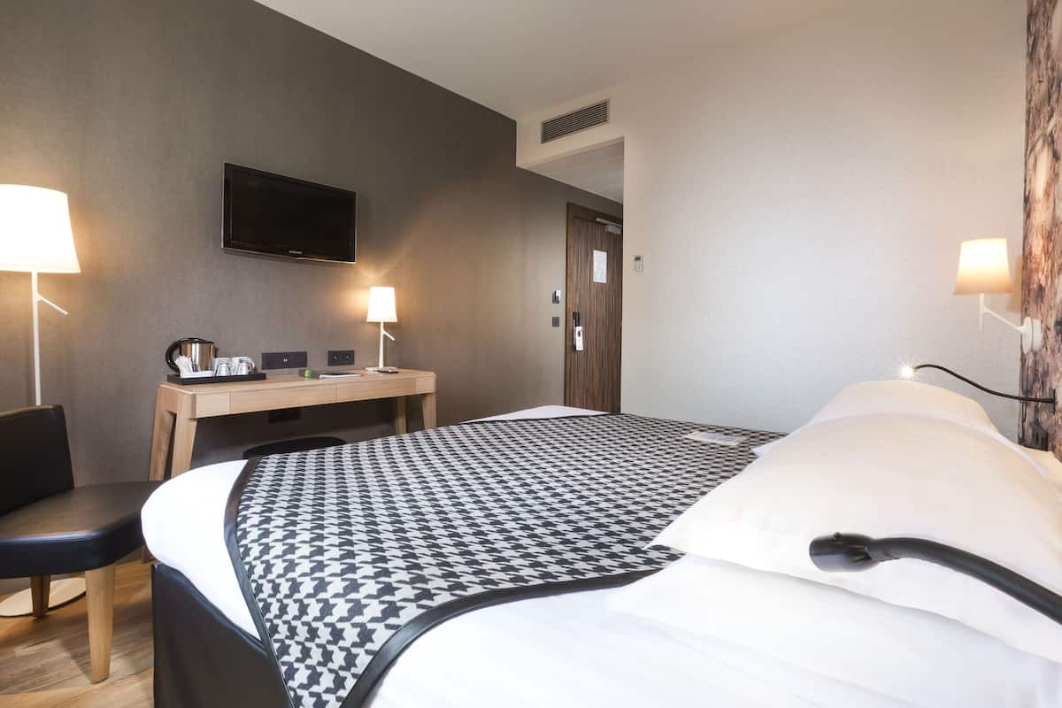A hotel room with a bed, a desk, a chair, a television, and two lamps.
