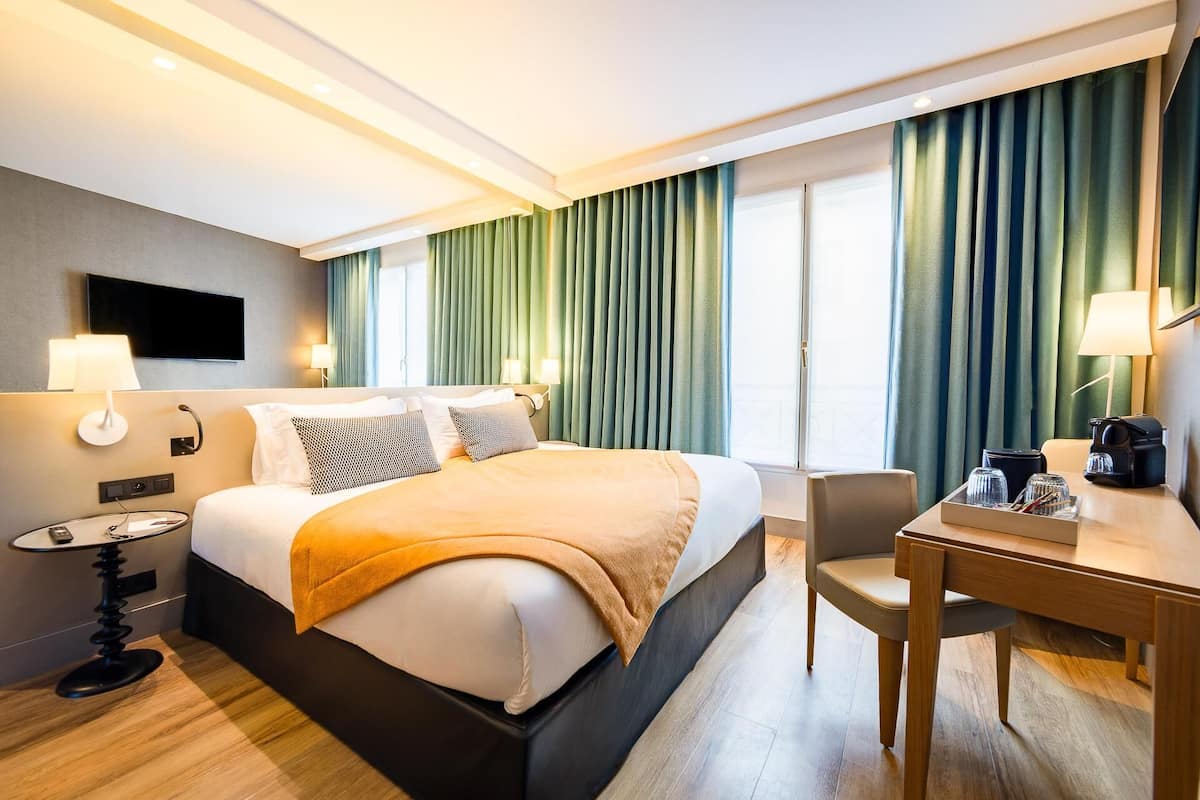 A hotel room with a bed, bedside tables, a desk, and a chair.