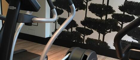 A stationary bike with a digital display, a wall with a tree pattern, and a wooden floor.