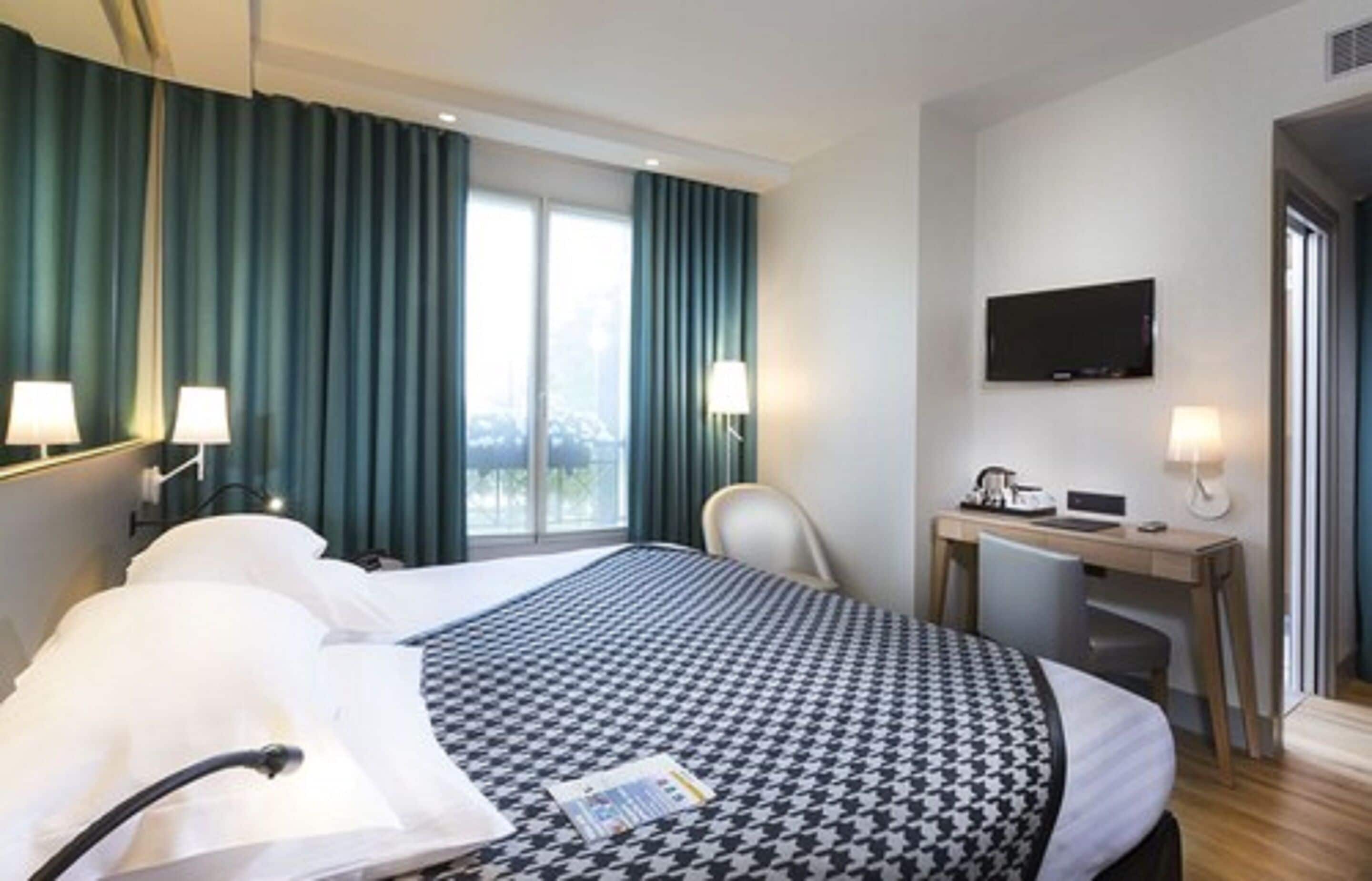 Une chambre d’hôtel avec un grand lit, un bureau, une chaise, une télévision et une fenêtre avec des rideaux.