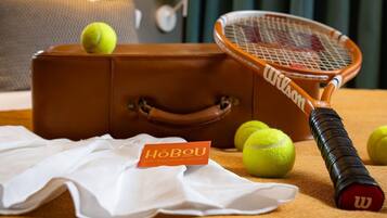 Une raquette de tennis, une valise et des balles de tennis sur un lit, avec une enseigne d’hôtel en arrière-plan.