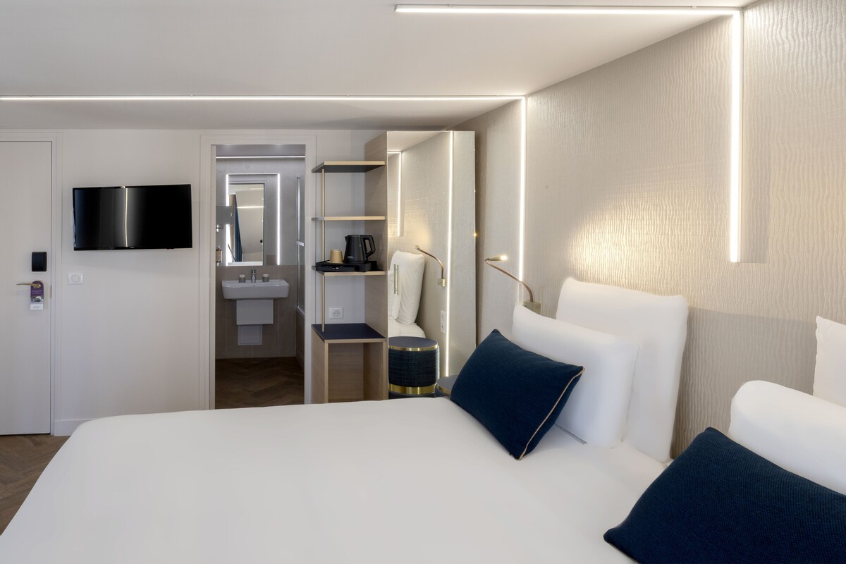 A modern hotel room with a large bed, a flat-screen TV, a bedside table, and a built-in wardrobe.