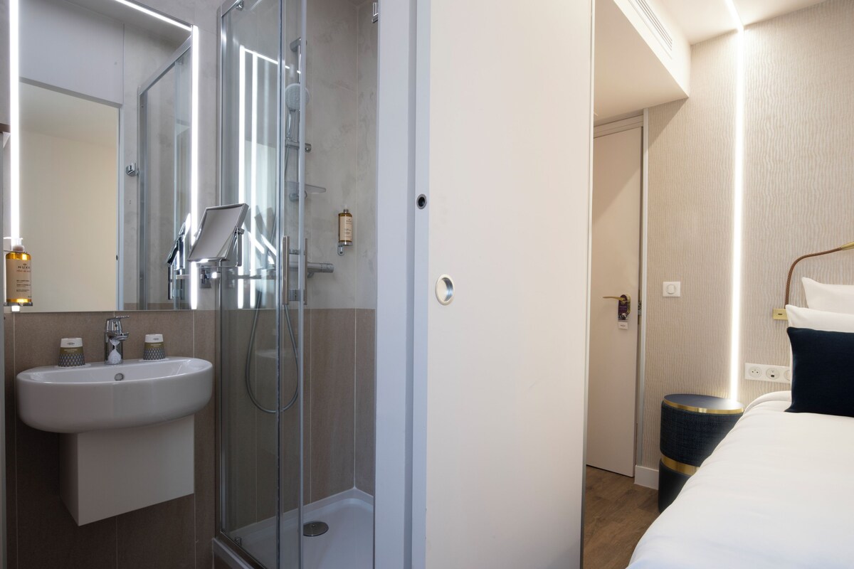 A hotel bathroom with a glass-enclosed shower, a sink, and toiletries.