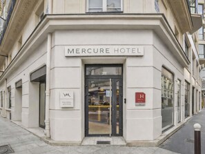 The exterior of the Mercure Hotel with a classic facade, a prominent entrance, and a sign indicating the hotel name. - Mercure Paris Opera Lafayette (Paris)