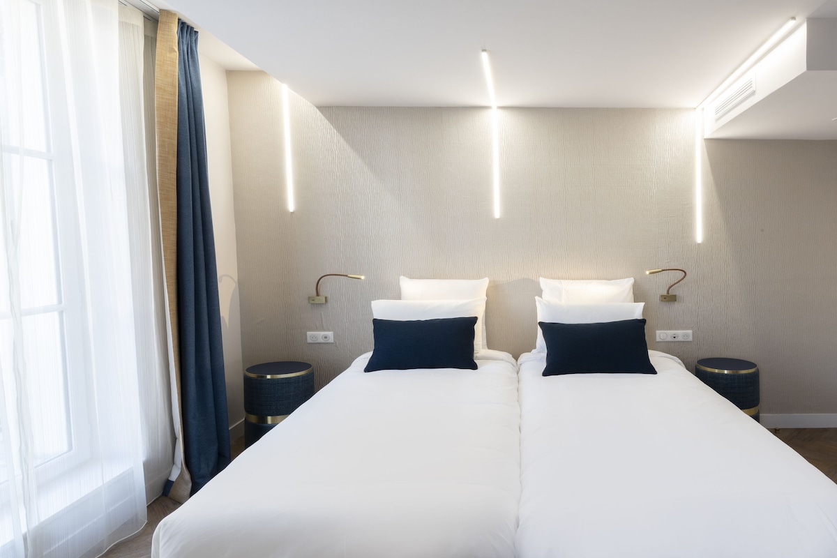 A hotel room with a double bed, two bedside tables, and a large window with curtains.