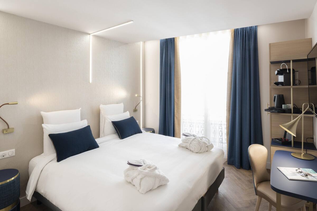 A hotel room with a bed, bedside tables, a desk, and a chair.