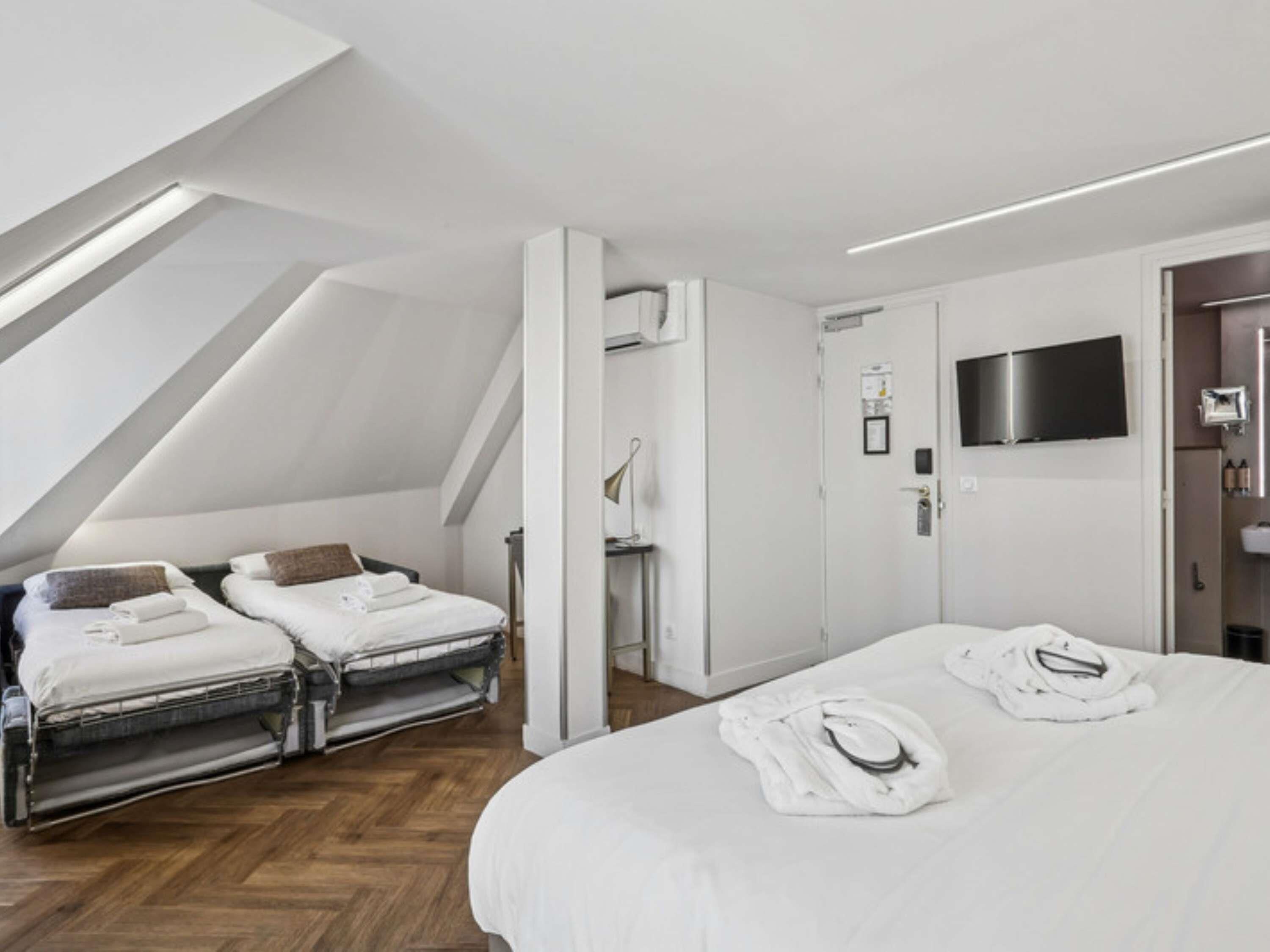 Une chambre d’hôtel comprenant un lit, deux tables de chevet, un téléviseur à écran plat et un plafond doté de lucarnes.