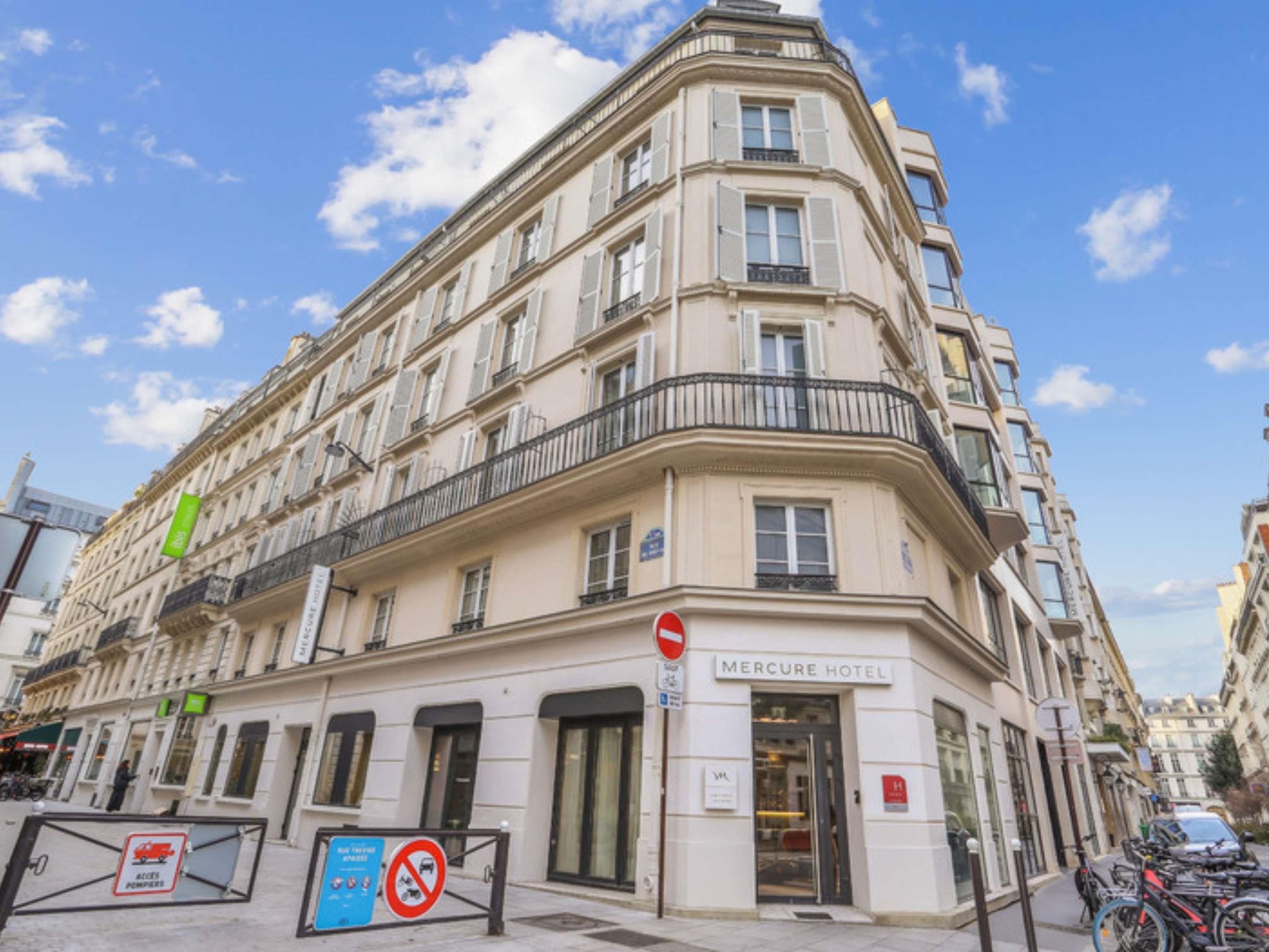 Un immeuble d’angle avec une enseigne indiquant « Hôtel Mercure » et un panneau interdisant le stationnement.