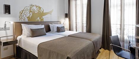 A hotel room with two beds, a desk with a chair, a wall-mounted lamp, and a large window with curtains.