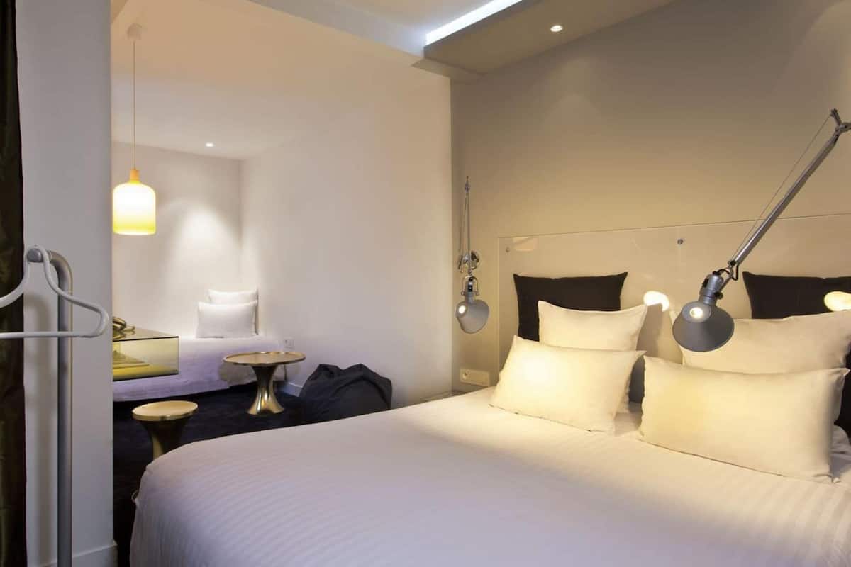 Una habitación de hotel con una cama, lámparas de noche, una mesita redonda y un candelabro colgante.