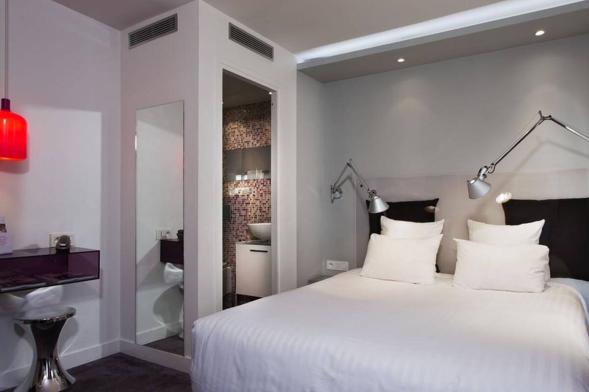 Una habitación de hotel moderna con una cama grande, un escritorio y un baño visible a través de una puerta abierta.