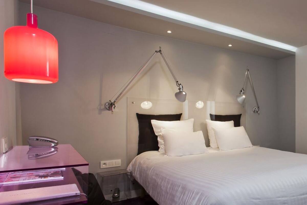 Una habitación de hotel moderna con una cama, lámparas de noche, un escritorio y una lámpara colgante roja.