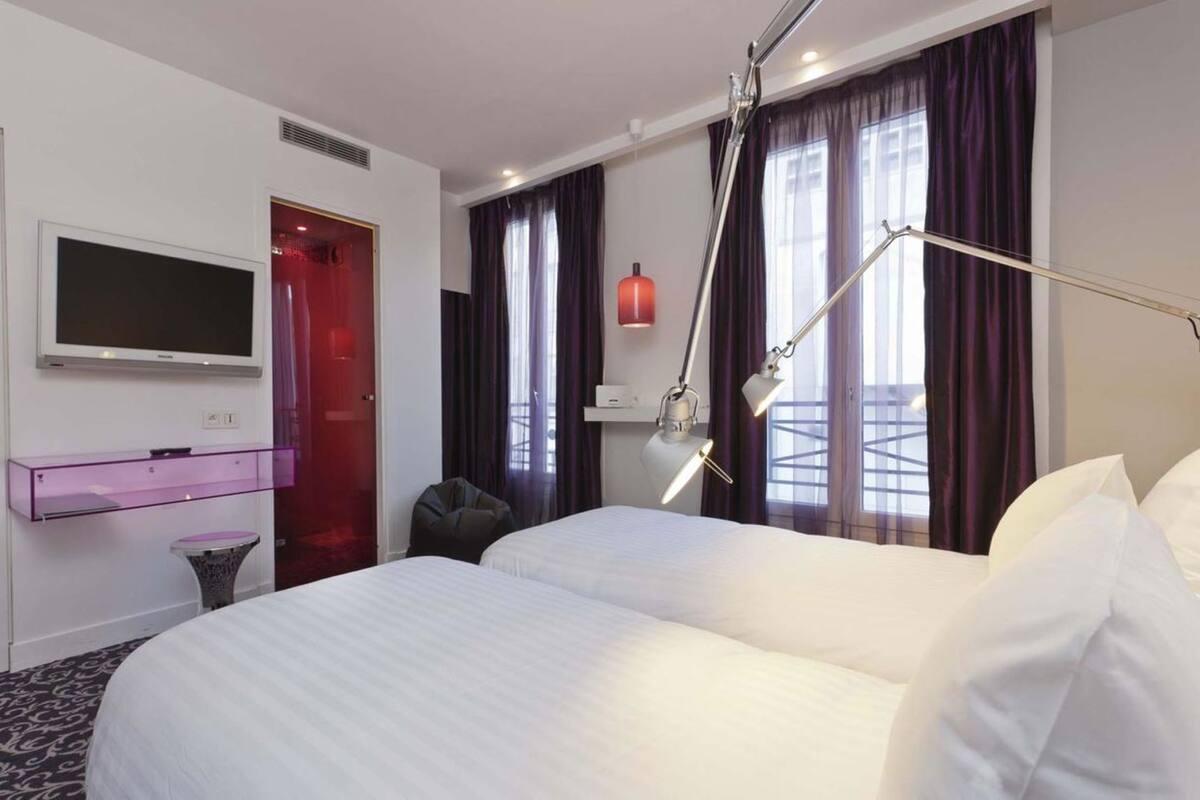 Una habitación de hotel con cama, televisión, escritorio y ventana con cortinas.