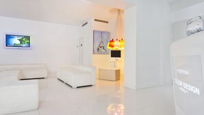 A modern hotel reception area with a white color scheme, a reception desk, a flat-screen TV, and a wall-mounted artwork.