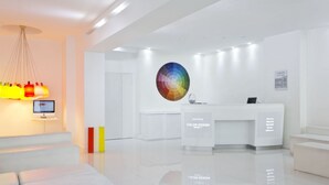 A modern hotel reception area with a white color scheme, a reception desk, and a large circular wall art piece.