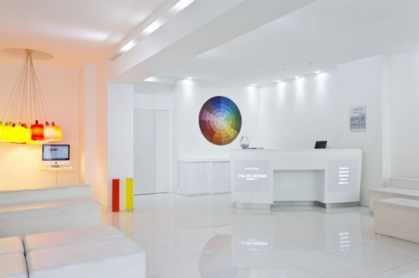A modern hotel reception area with a white color scheme, a reception desk, and a large circular wall art piece.