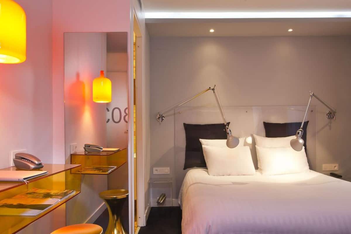 Habitación de hotel con cama, mesitas de noche, escritorio, teléfono y espejo.