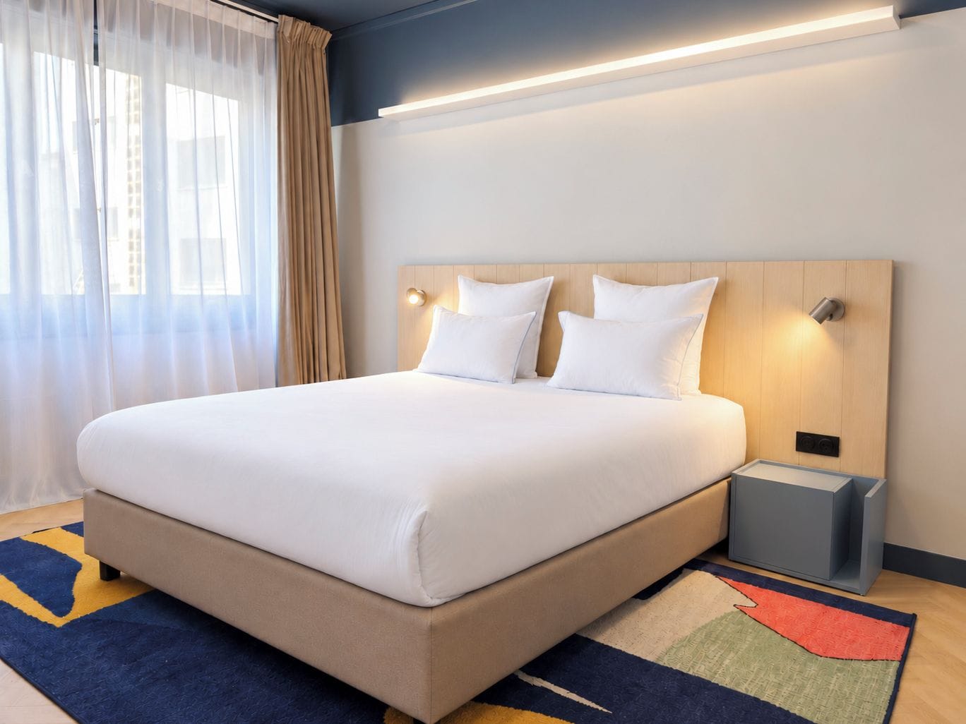 A hotel room with a large bed, a bedside table, a nightstand, and a window with curtains.