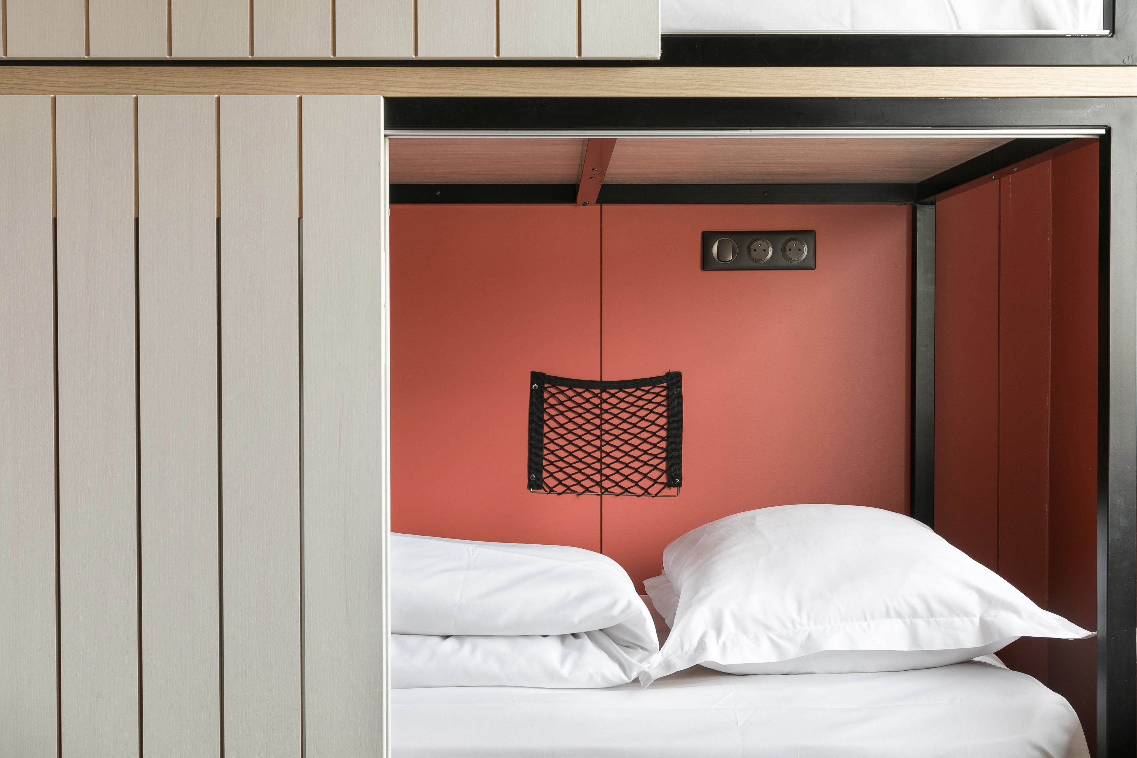 Une petite pièce comprenant un lit, une étagère et un luminaire fixé au mur.