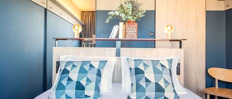 A modern hotel room with a bed, geometric patterned pillows, a vase with flowers, and bedside lamps.