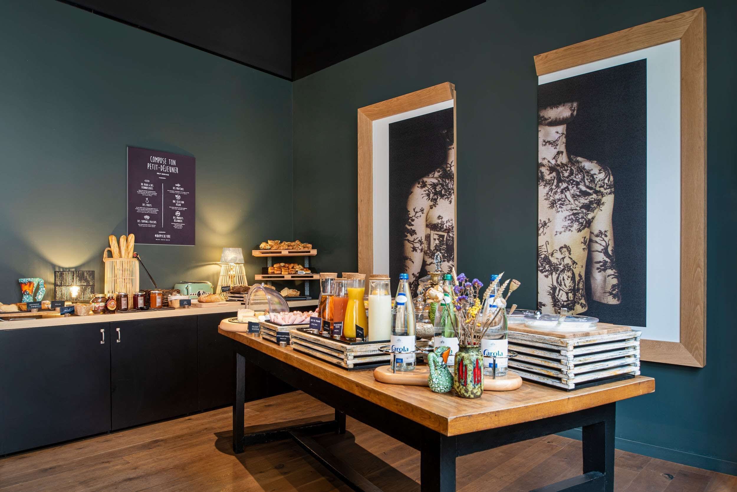 Un buffet per la colazione con diversi cibi e bevande, opere d'arte appese al muro e una bacheca con il menù.
