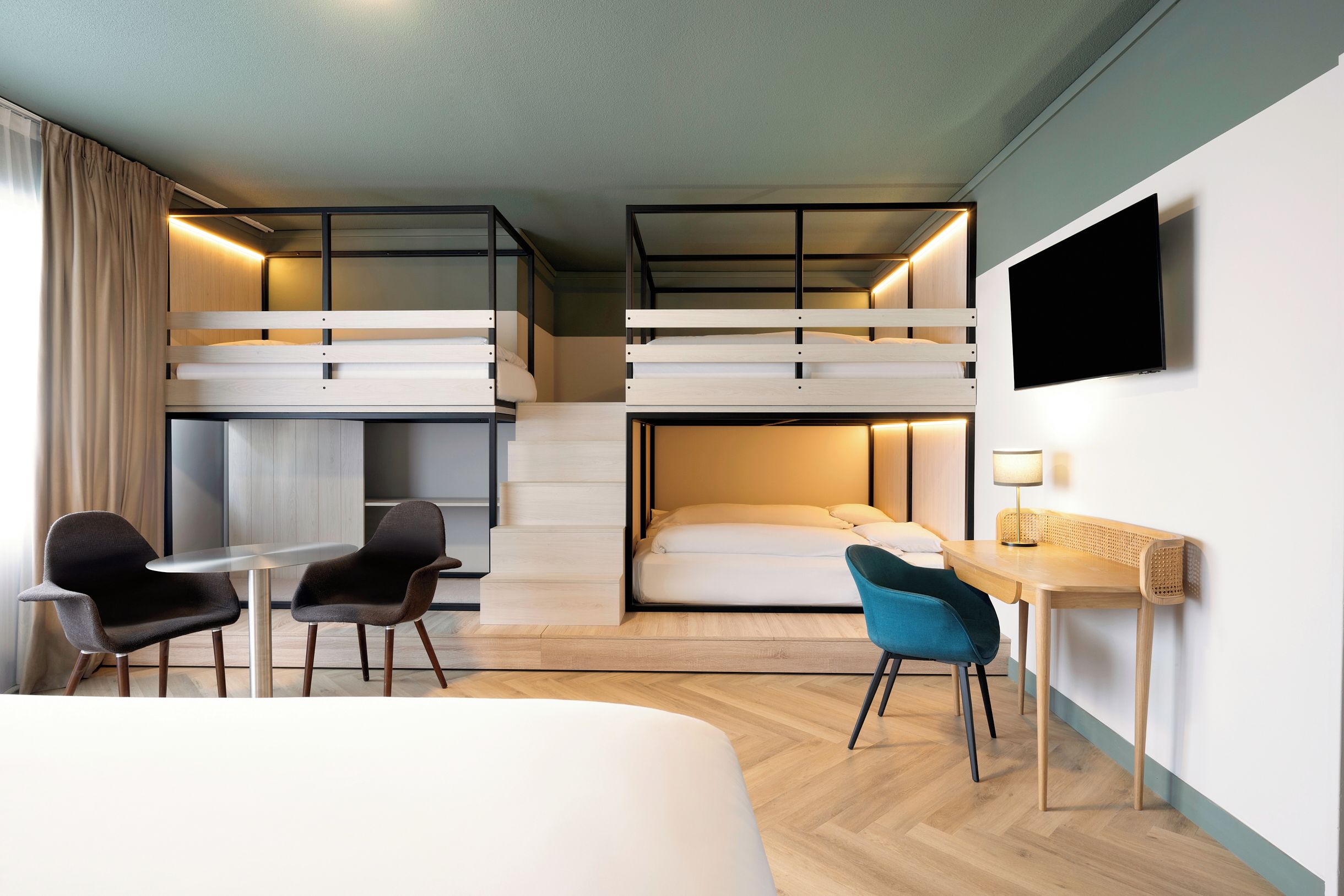 A hotel room with bunk beds, a desk, a chair, a TV, and a staircase.