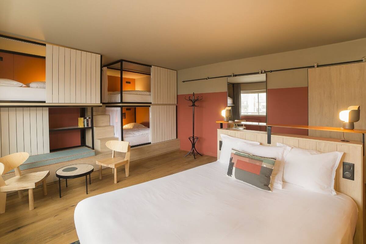 Ein Hotelzimmer mit einem großen Bett, einem Schreibtisch, zwei Stühlen, einem Kleiderständer und einem Spiegel.