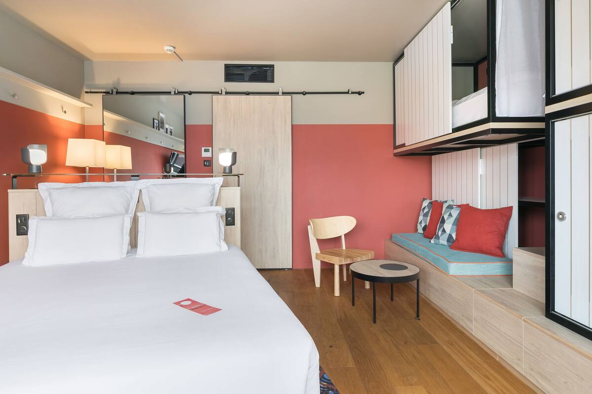 Ein Hotelzimmer mit einem großen Bett, einem kleinen Tisch, einem Sessel, einer Couch, einem Spiegel und einem Kleiderschrank.