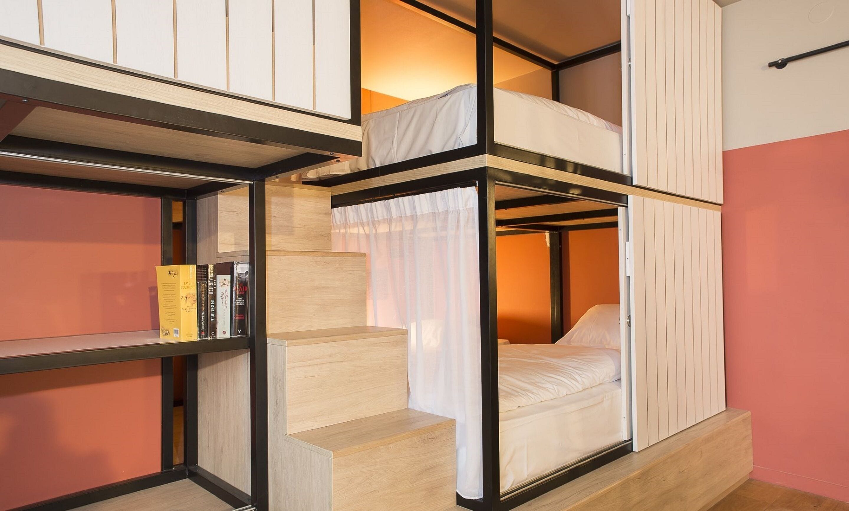 A bunk bed room with a wooden ladder, a shelf with books, and a curtain.