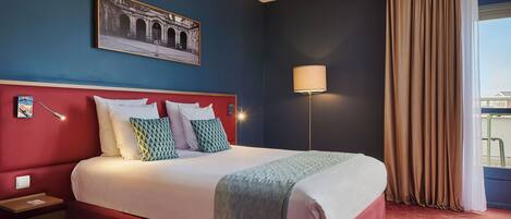 A hotel room with a large bed, a nightstand, a lamp, a window with curtains, and a framed picture on the wall.