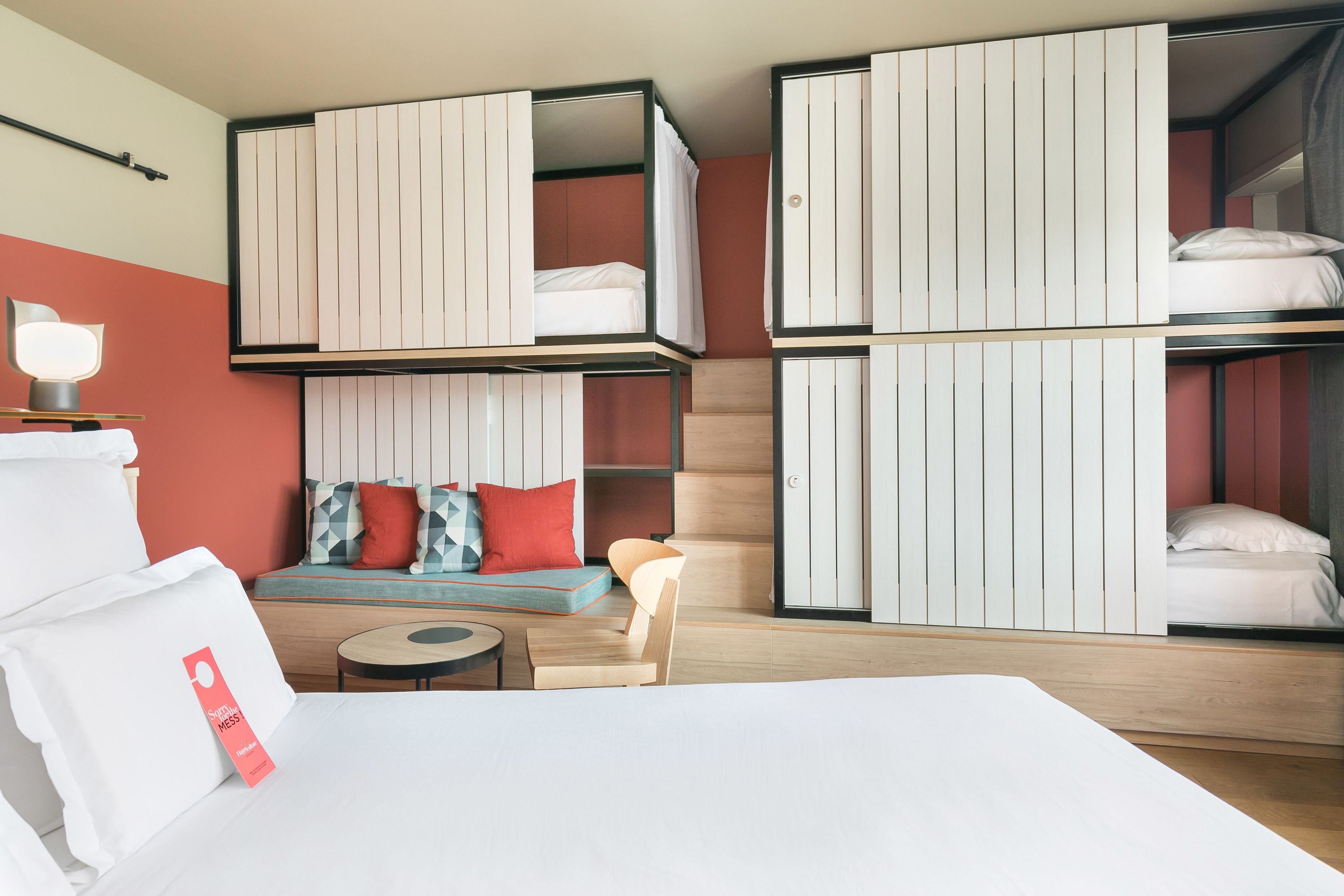 Ein modernes Hotelzimmer mit einem großen Bett, einer Sitzecke mit Kissen, einem kleinen Tisch und integrierten Schränken.