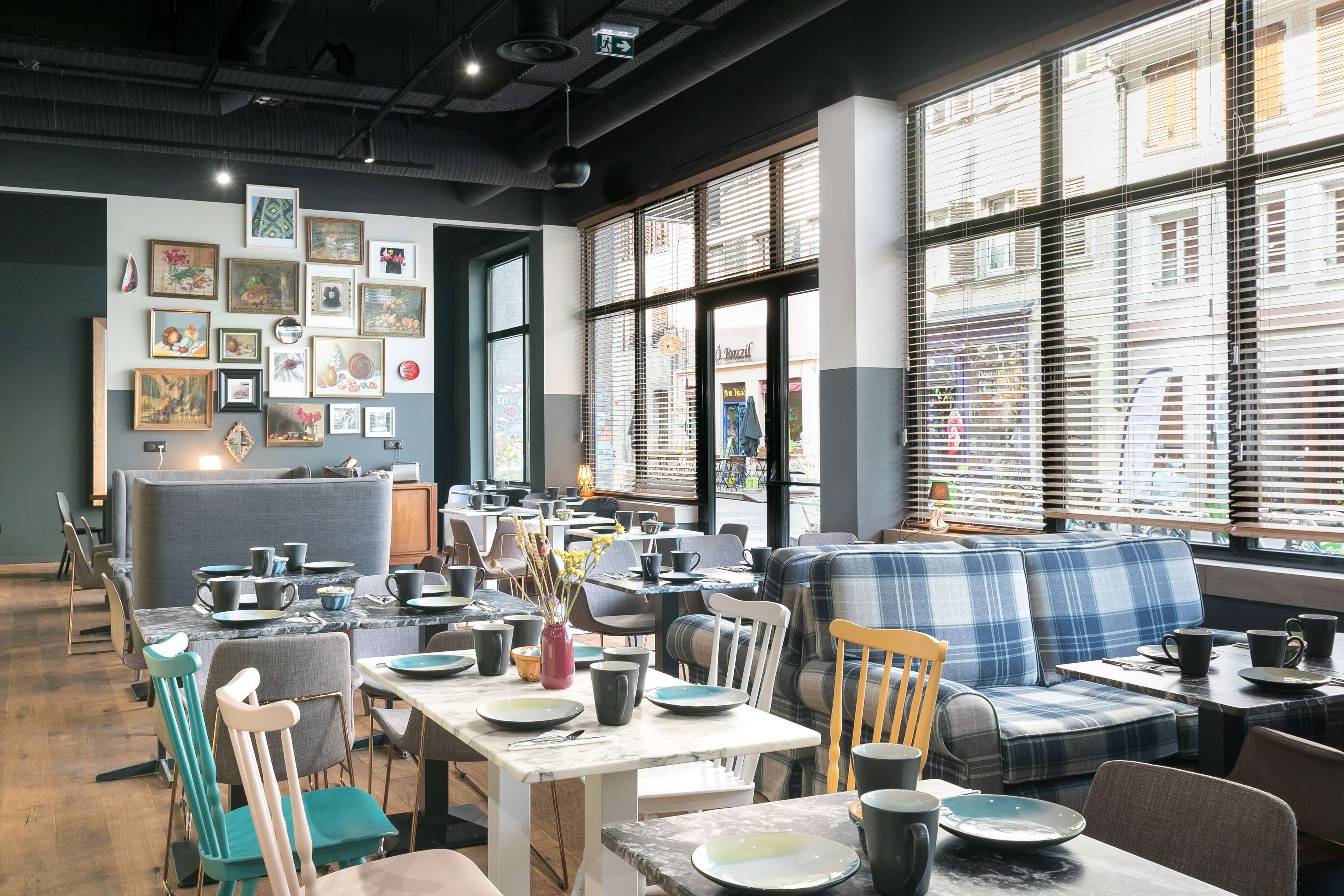 Ein modernes Café mit Tischen, Stühlen und einer Couch, ausgestattet mit großen Fenstern und Jalousien.