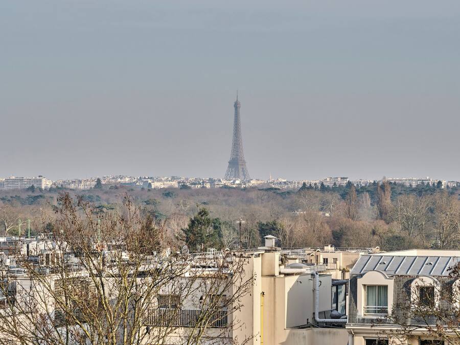 Uitzicht op de Eiffeltoren in de verte, met gebouwen op de voorgrond en een mistige lucht.