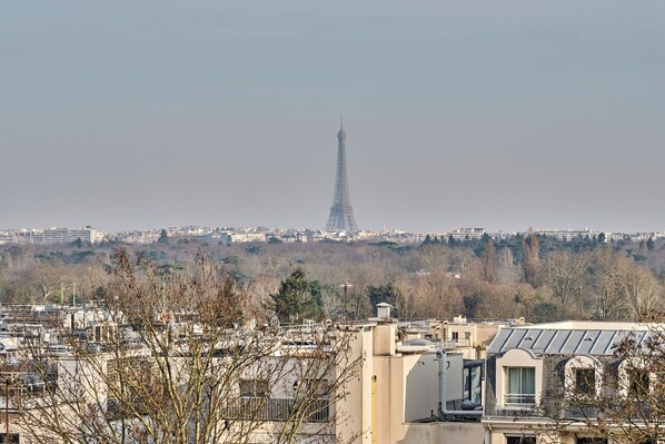 Une vue de la Tour Eiffel prise de loin, avec des bâtiments au premier plan et un ciel brumeux.