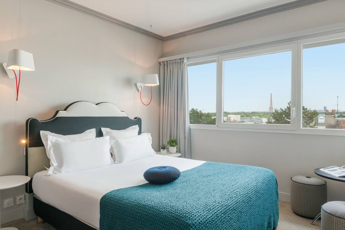 A hotel room with a large bed, a view of the Eiffel Tower, a small table, and a lamp.