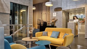 A modern hotel lobby with a yellow sofa, blue armchairs, and a small round table. - Hotel Atrium by HappyCulture (Suresnes)