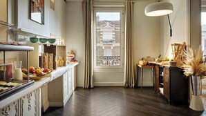 A hotel room with a breakfast bar, a large window with curtains, a view of buildings outside, and a modern lamp. - Hotel Atrium by HappyCulture (Suresnes)