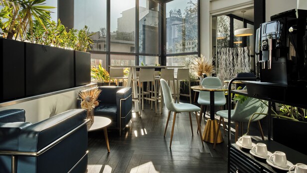 A modern cafe with a high ceiling, large windows, and a variety of seating options including sofas and chairs. - Hotel Atrium by HappyCulture (Suresnes)