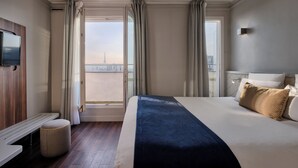 A hotel room with a bed, a TV, a bench, and a view of a cityscape. - Hotel Atrium by HappyCulture (Suresnes)