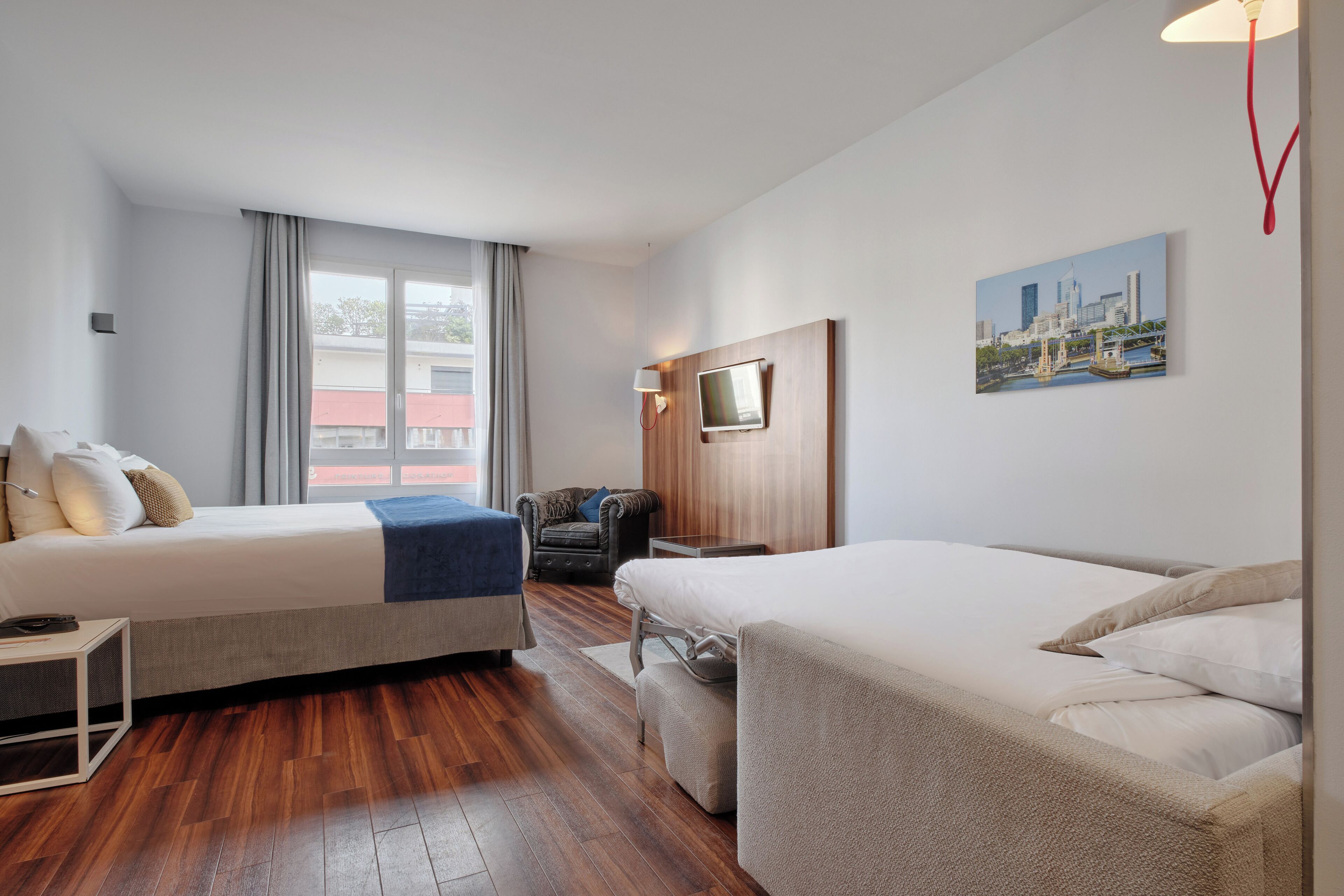 Habitación de hotel con dos camas, televisión, una silla y un cuadro con vista a la ciudad.