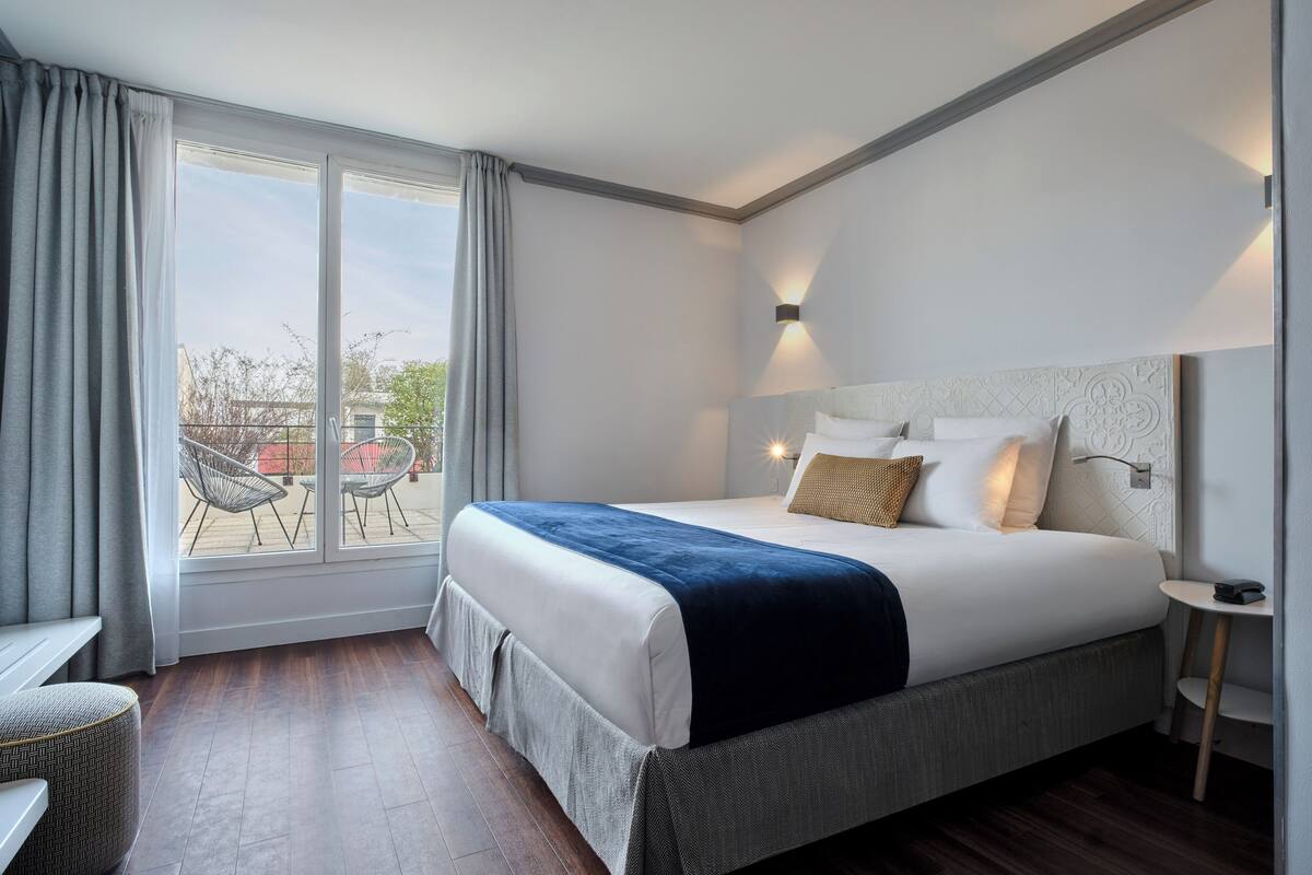 A modern hotel room with a large bed, a small table, and a view of the outside.