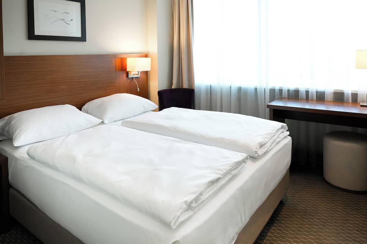 Ein Hotelzimmer mit zwei Betten, einem Schreibtisch, einem Stuhl und einer Lampe.