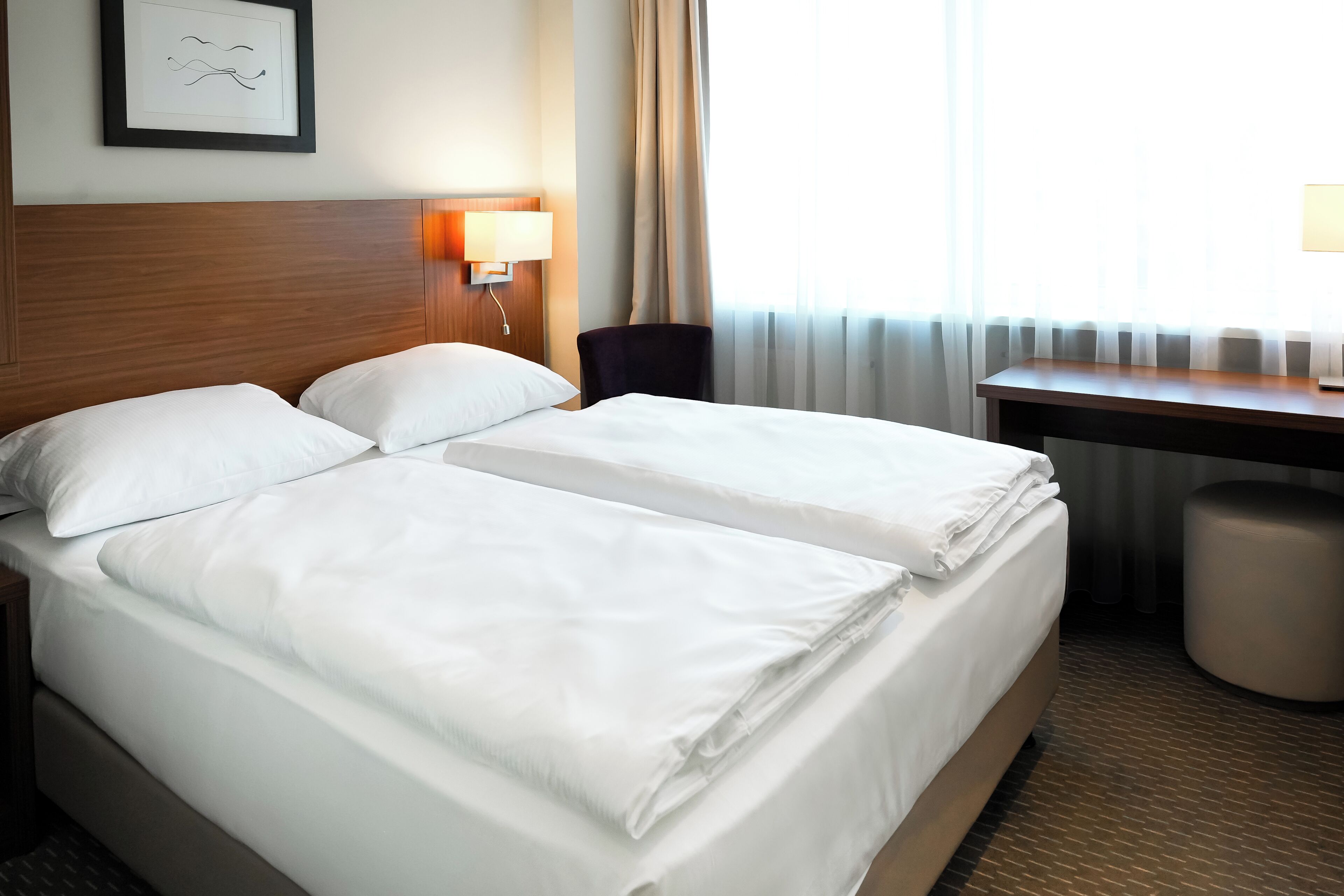 A hotel room with two beds, a desk, a chair, and a lamp.
