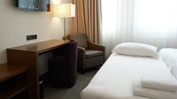 Una habitación de hotel con una cama, un escritorio, una silla, una lámpara y un televisor en la pared.