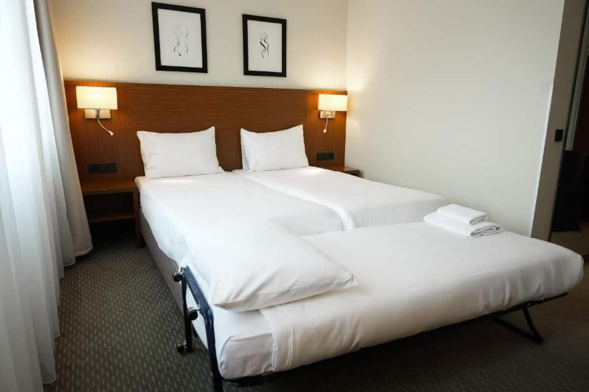 Ein Hotelzimmer mit einem Doppelbett, zwei Nachttischen, Wandlampen und gerahmten Bildern an der Wand.