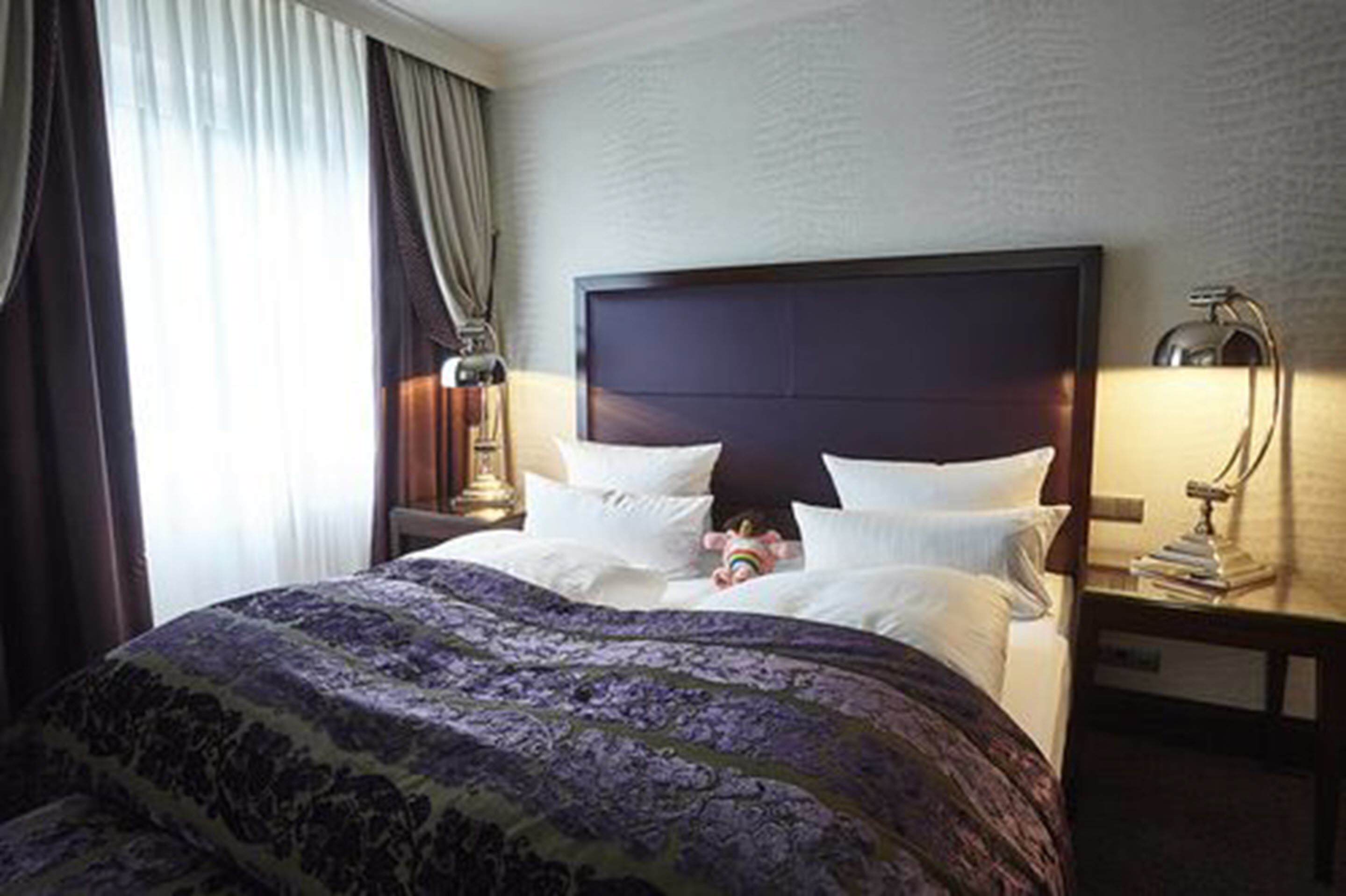 Una camera d'albergo con un letto grande, un comodino con una lampada e una finestra con tende.
